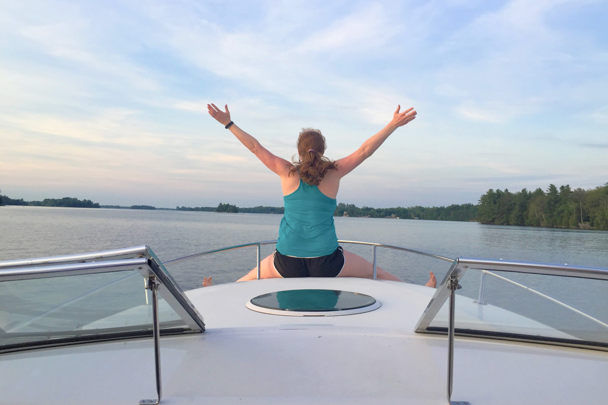 Dressed in casual outfits, stem cell donor Rachel Van Pelt sits at the tip of a boat with her hands up in the air as she enjoys the peaceful atmosphere.