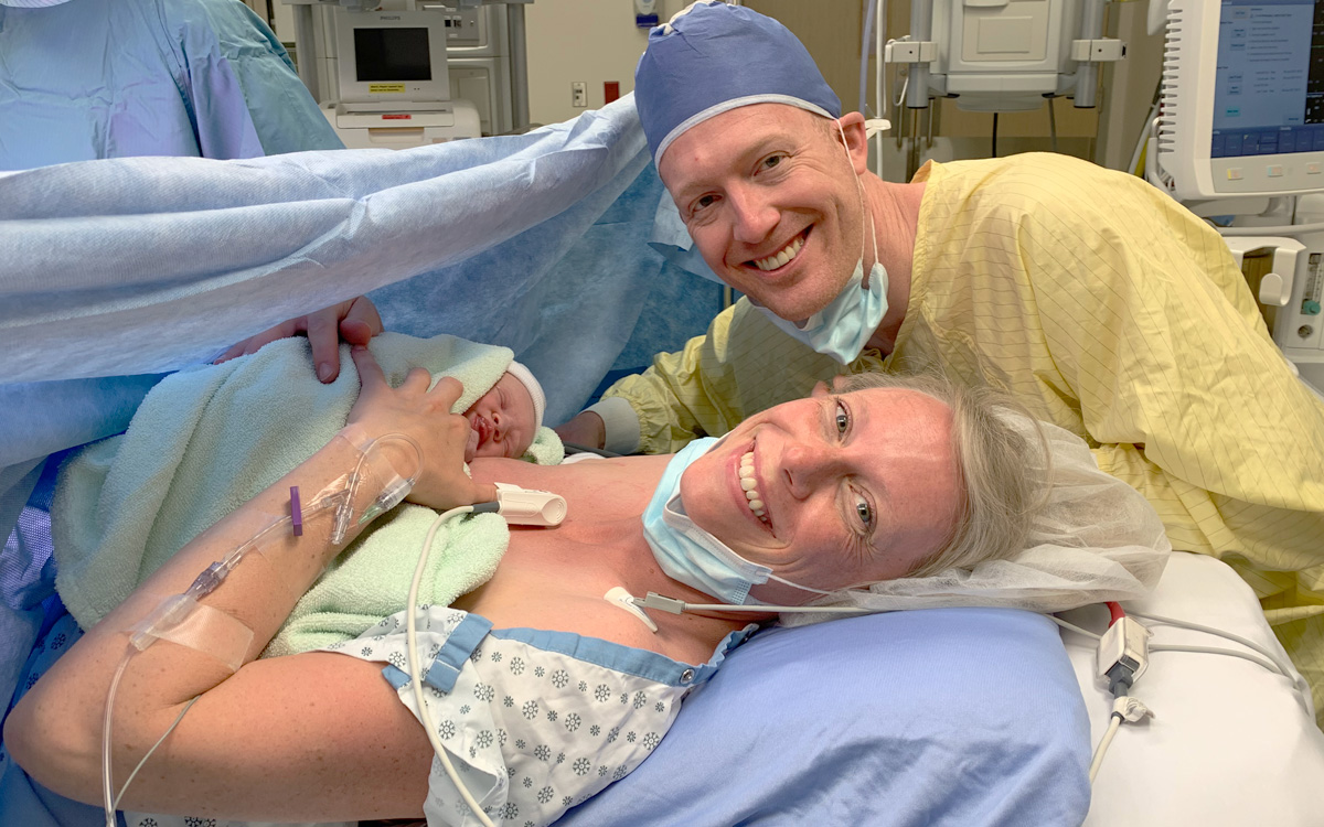 Rebecca and Tyler Munk smile in hospital gowns, with baby Eliza on Rebecca’s chest minutes after she was born.