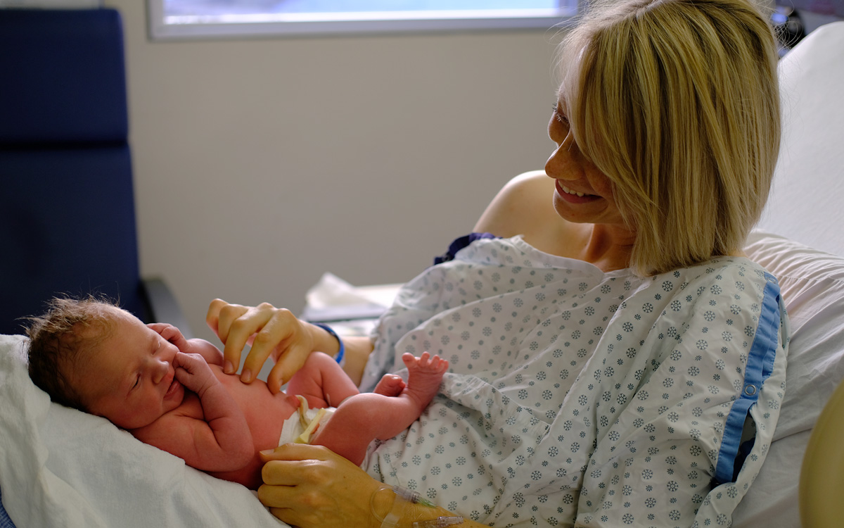 Sitting on her hospital bed, cord blood donor Rebecca Munk smiles as she tickles her newborn baby, Eliza Munk.