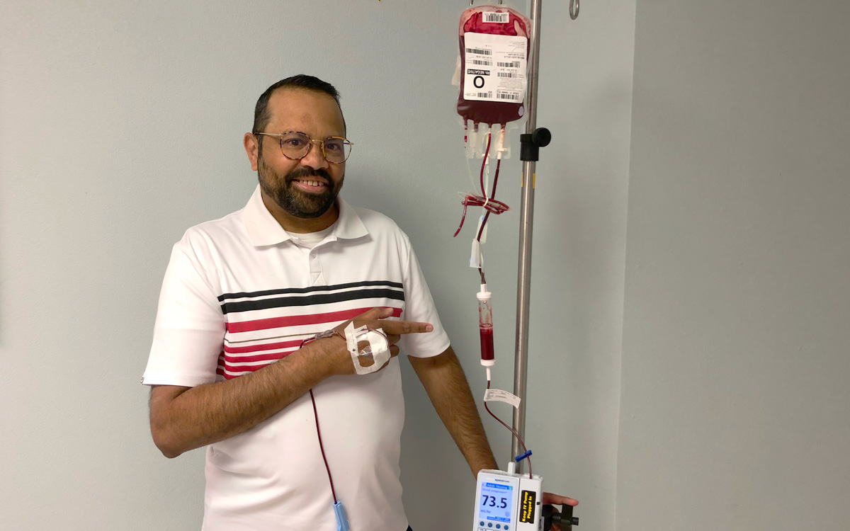Salim Amlani stands while receiving a transfusion at Foothills Medical Centre and points at the intravenous sending the blood to his body