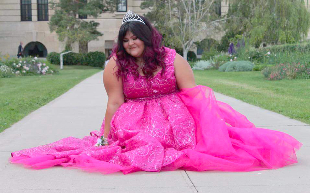 Shanelle Johnson sits on a paved walkway in a flowing pink dress.