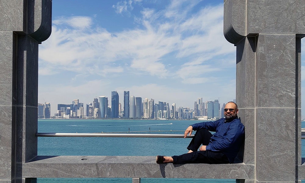 Man sitting on structure with Doha skyline in background