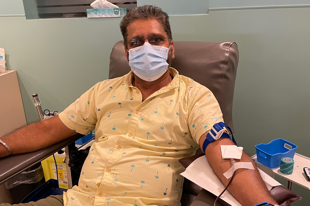 Adult male wearing a mask covering his nose and mouth on a bed donating blood