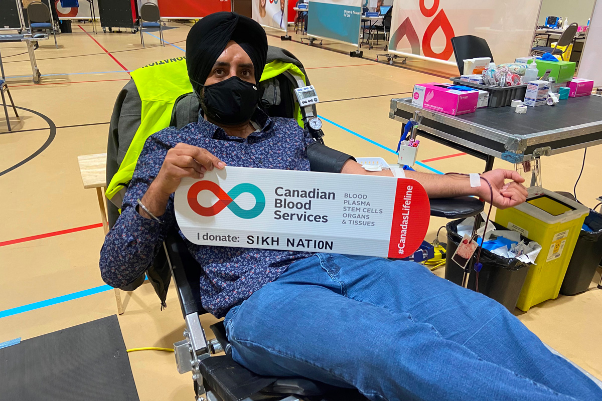 Adult male wearing a mask covering his nose and mouth on a bed donating blood