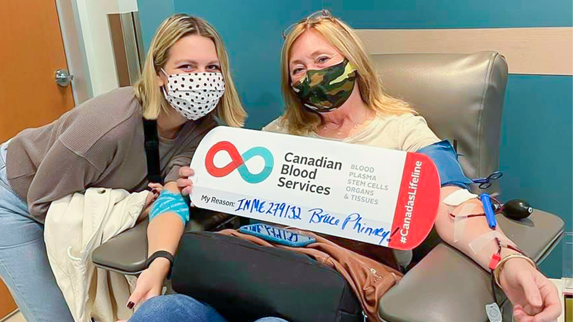 A blonde mother donating blood sitting in a donation chair at the donor centre along with her daughter