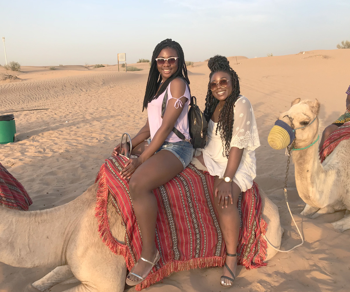 Two young girls on a camel in the desert