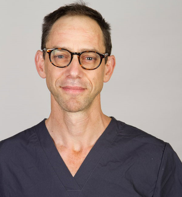 Man in scrubs wearing glasses looking into camera