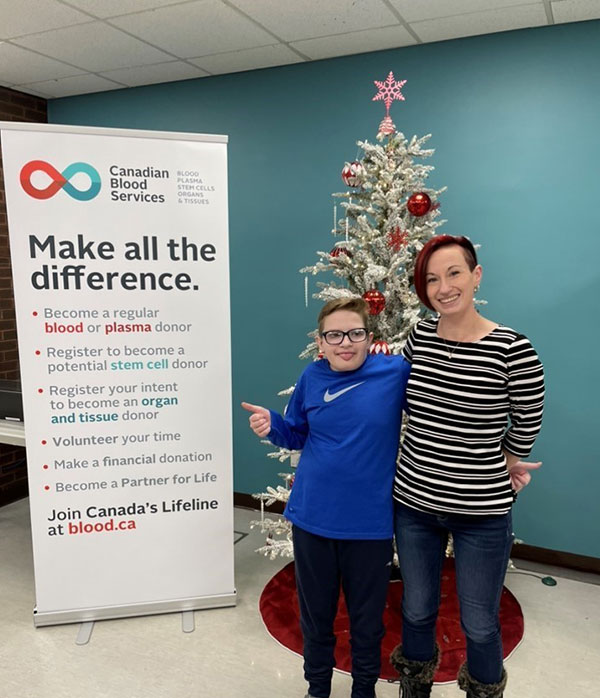 Mother and son inside Canadian Blood Services donor centre next to a banner that says, “Make all the difference.”