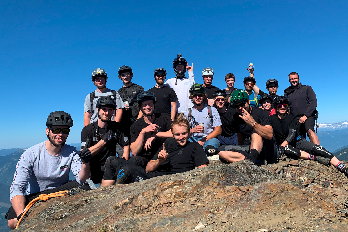 Team photo of bike staff in helmets atop a ridge with mountains in the background