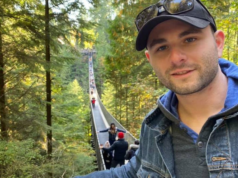 Blood recipient, Ben Becker, in front of suspension bridge in forest