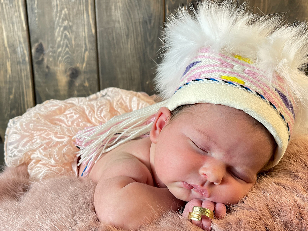 Tiny baby wearing feathery hat sleeping on fur