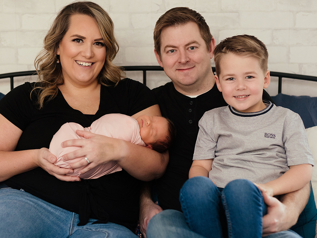 Family of four cuddling together on bed