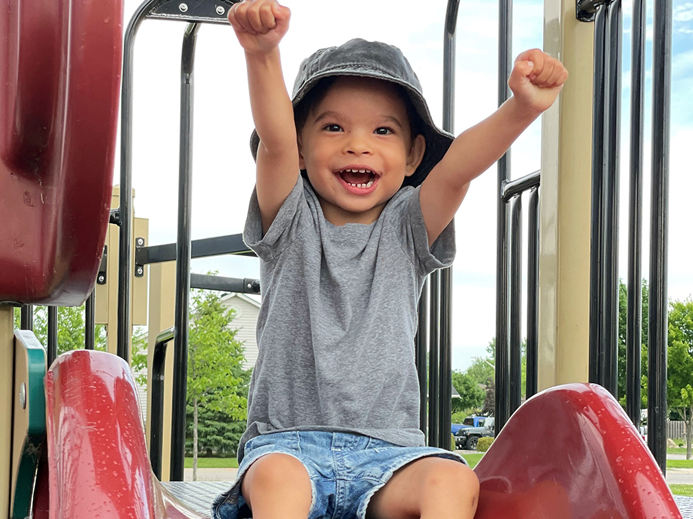 Boy smiling arms outstretched at top of red slide