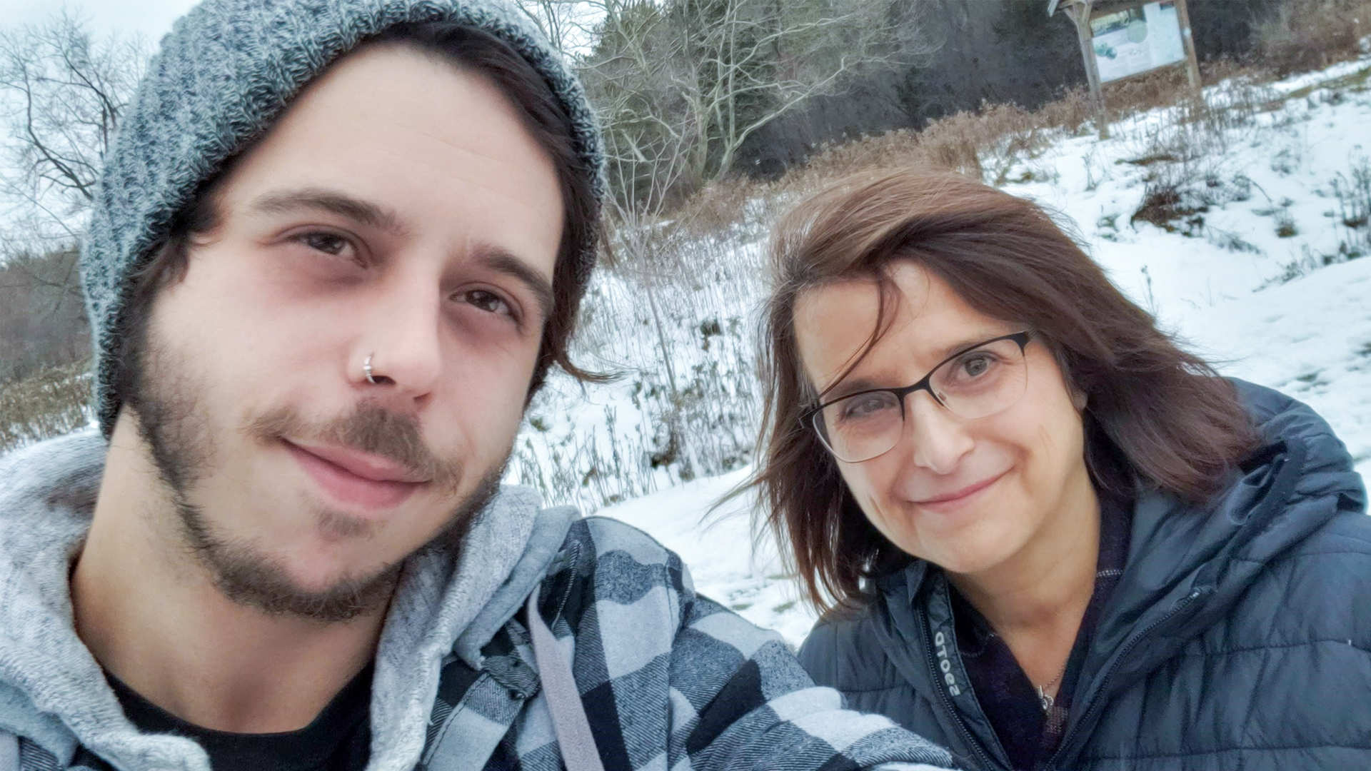 A mother and her adult son take a selfie on a trail covered in snow.