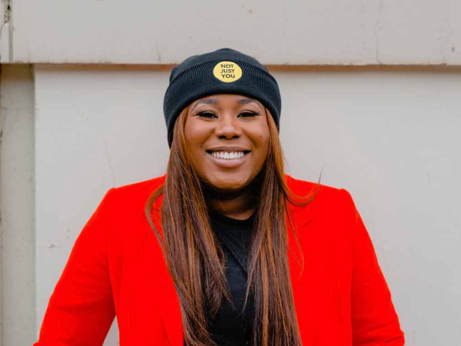 Woman in red jacket and beanie with a logo that says &quot;not just you&quot;