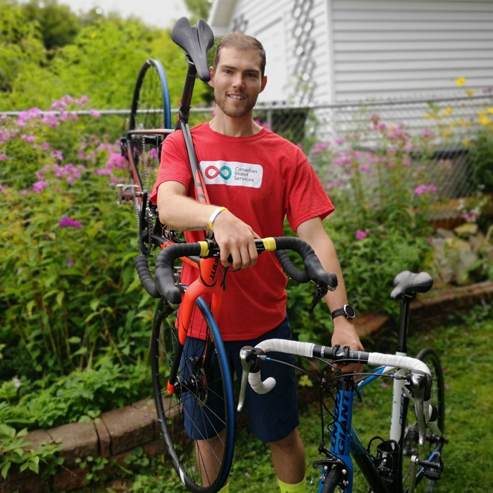 Young person holding a bike over his shoulder, wearing a Canadian Blood Services t-shirt