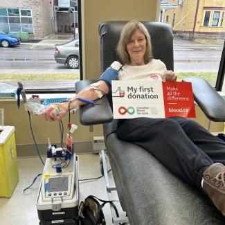 Blood donor in chair holding sign that says my first donation