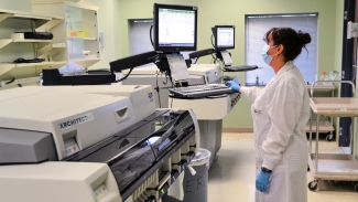 Image of Senior medical lab technologist Valerie Conrod standing in front of the large machine to test samples