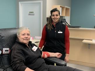 Robenpreet Sooch standing with Patricia Hanson in chair donating blood