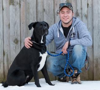 Scott Monds, who had two stem cell transplants from a single donor, crouches with his arm around his black and white dog, Beau