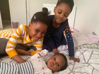 two sisters who suffered from sickle cell anemia on a bed with their infant sister