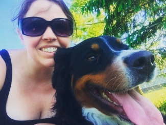 A medium-sized, black, brown and white dog with its pink tongue lolling out, and a woman wearing sunglasses.