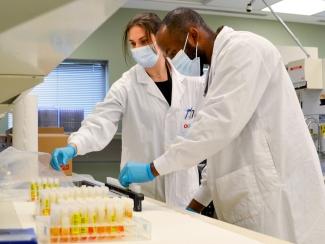 Image of Carissa Kohnen and Andy Tshiula Kalenga prepare samples for testing wearing masks and ppe.