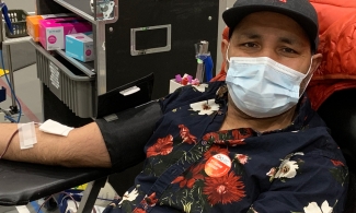 A man with a black floral shirt sitting in a chair donating blood wearing a face mask at the donor centre in Calgary.