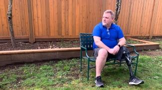 A man with a prosthetic leg sits on a bench outdoors.
