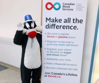 Blood donor in Sylvester the Cat costume and Happy New Year hat next to Canadian Blood Services sign