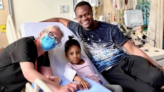 Aaliyah Mchopanga sitting in hospital bed surrounded with her father Abdi Mchopanga and registered nurse Kate Douglas 