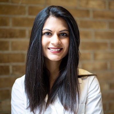 Woman with long black hair to the shoulders with a white shirt in front of a brick wall