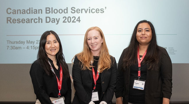 Three women standing together in front of a screen that says Canadian Blood Services' Research Day 2024