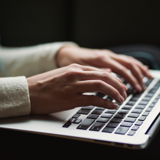 A woman's hands type on a laptop keyboard