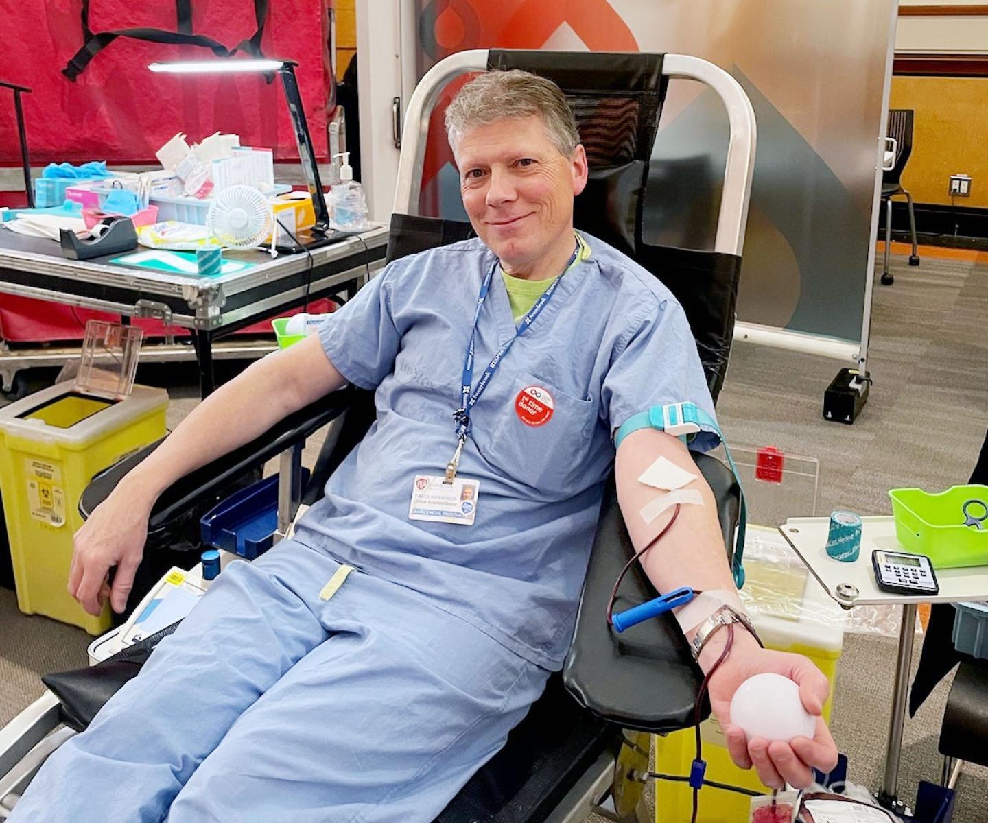 Man in blue scrubs and first-time donor sticker donated blood