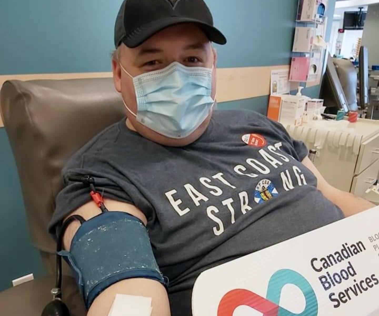 Man in ball cap and surgical mask donating blood