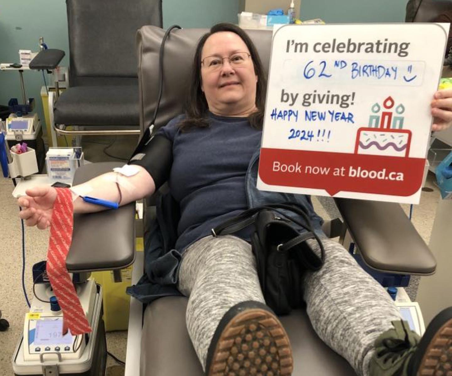 Donor giving blood while holding 62nd birthday sign