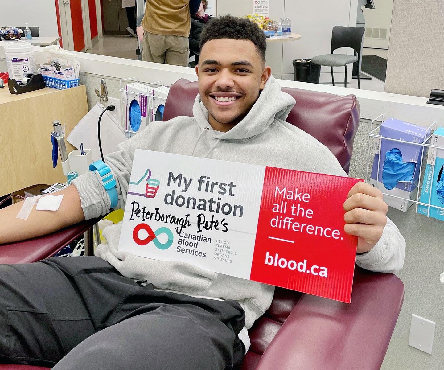 Blood donor in donor chair holding a “My first donation” sign