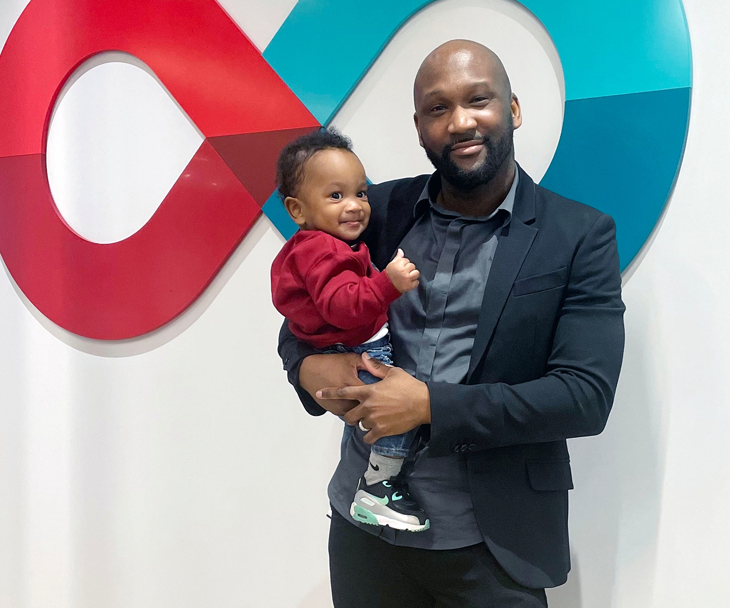 Blood donor holding his one-year-old son in front of Canadian Blood Services logo
