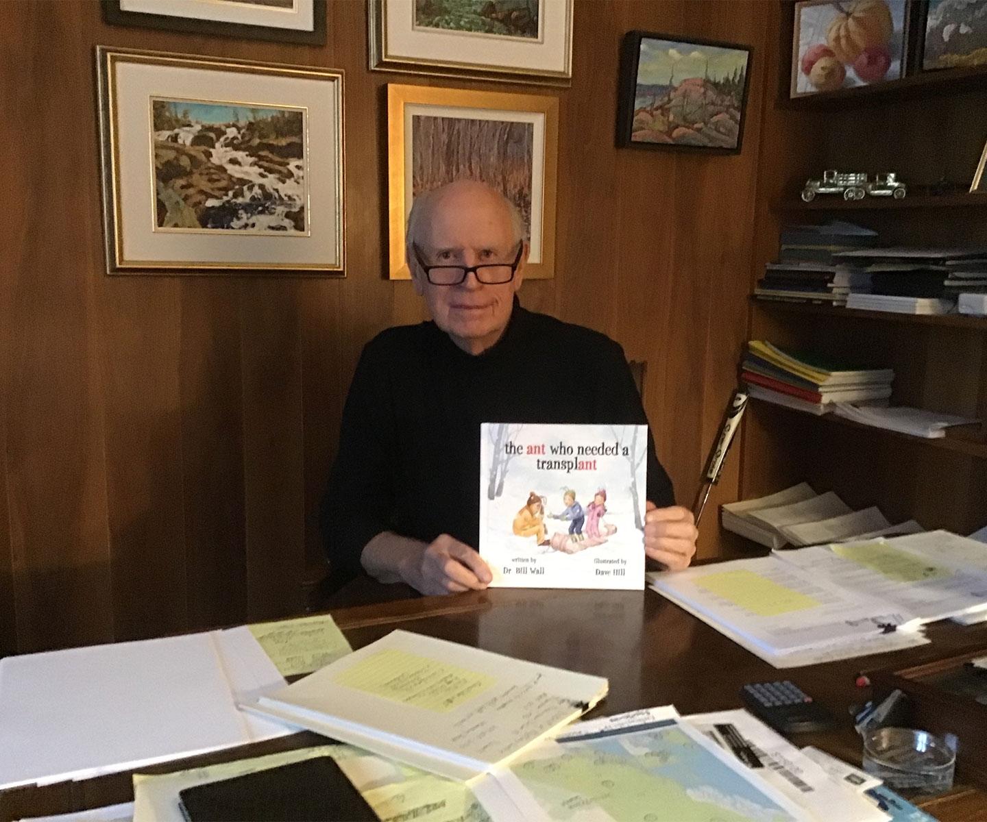 Dr. Wall sits at his desk displaying his children’s book the ant who needed a transplant.