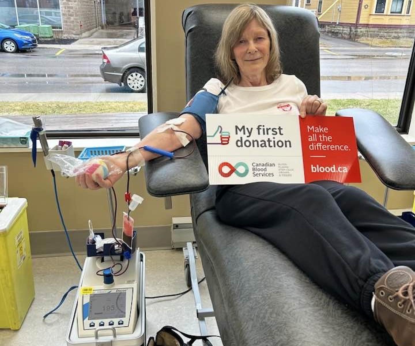 Blood donor in chair holding sign that says my first donation