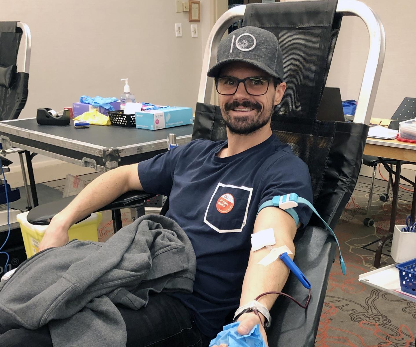 Man in baseball cap with first time donor sticker donating blood