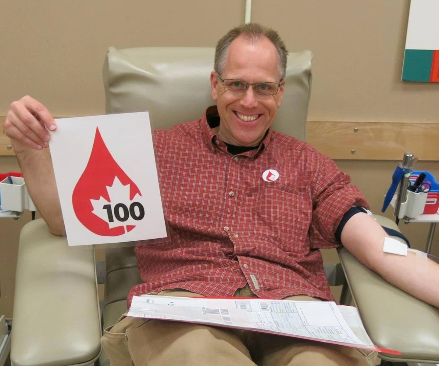 Blood donor holding sign featuring a blood drop and number 100
