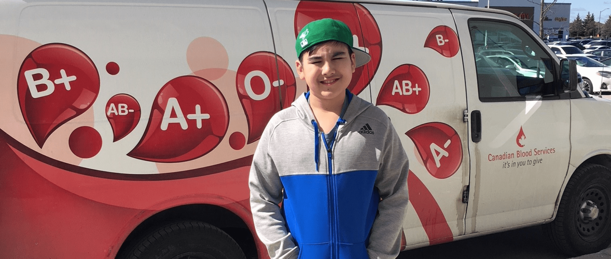 Aary with a green baseball cap standing in front of a Canadian Blood Services van outside