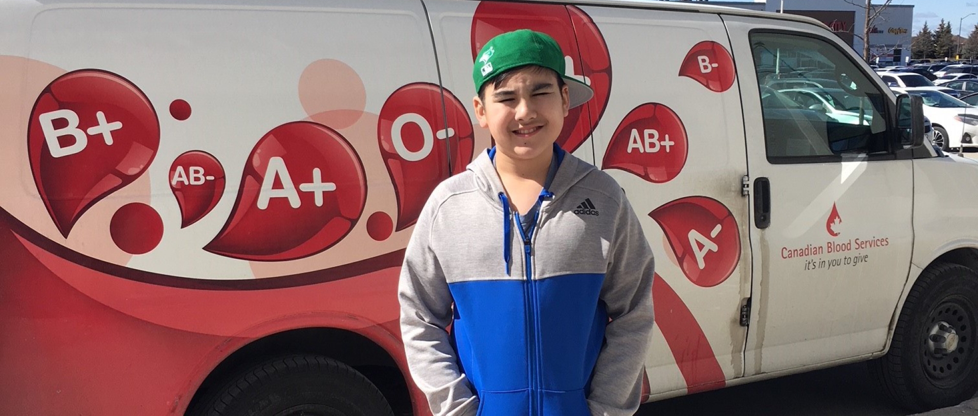 Aary with a green baseball cap standing in front of a Canadian Blood Services van outside