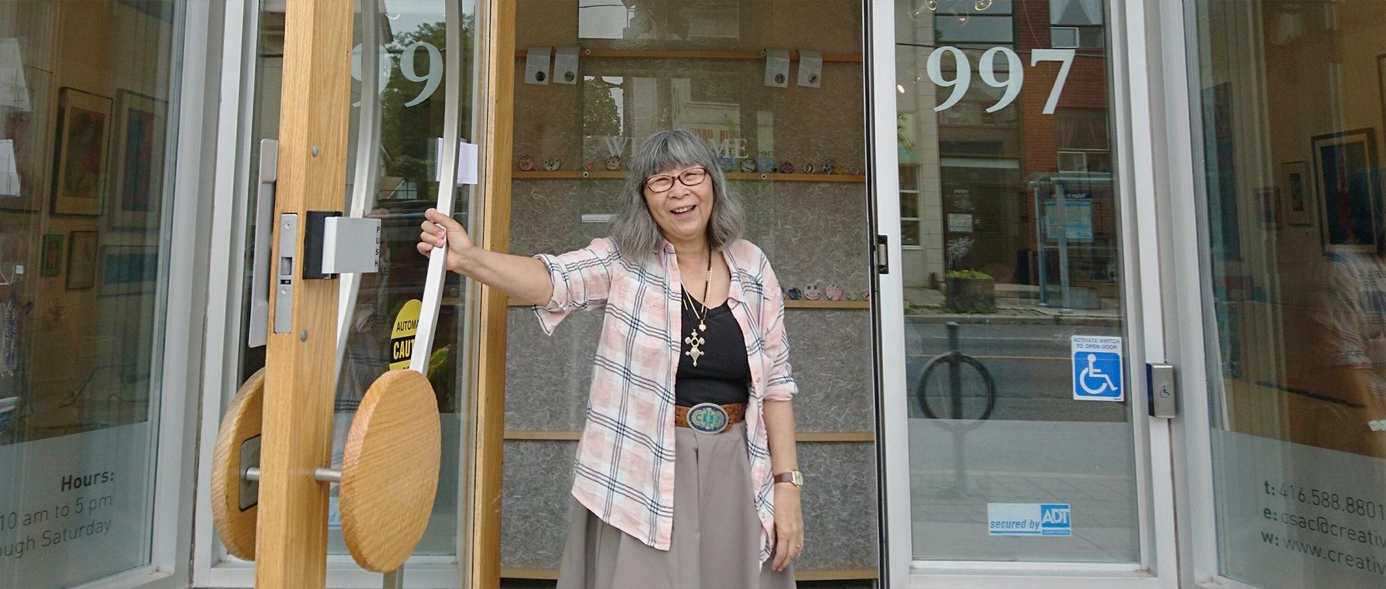 A woman smiles as she holds open the glass door to a building.