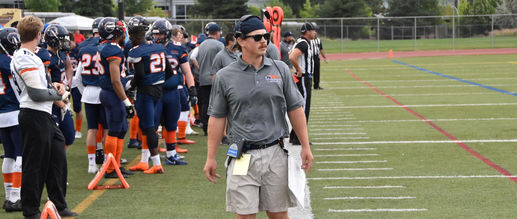 Braden Vankoughnett, head coach of the Kamloops Broncos Football Club and a recruiter of potential stem cell and blood donors, stands on the sidelines of a football game. 