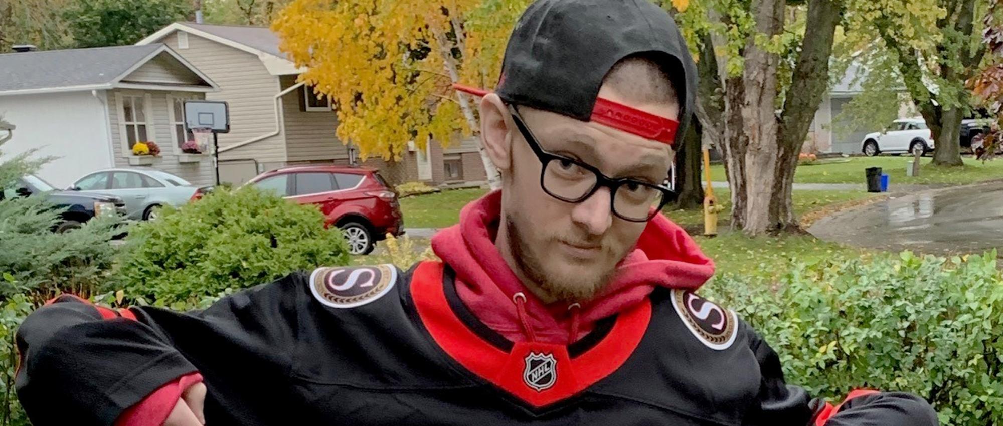 Image of Brian Fraser with black glasses wearing an Ottawa Senators jersey and a backwards cap.