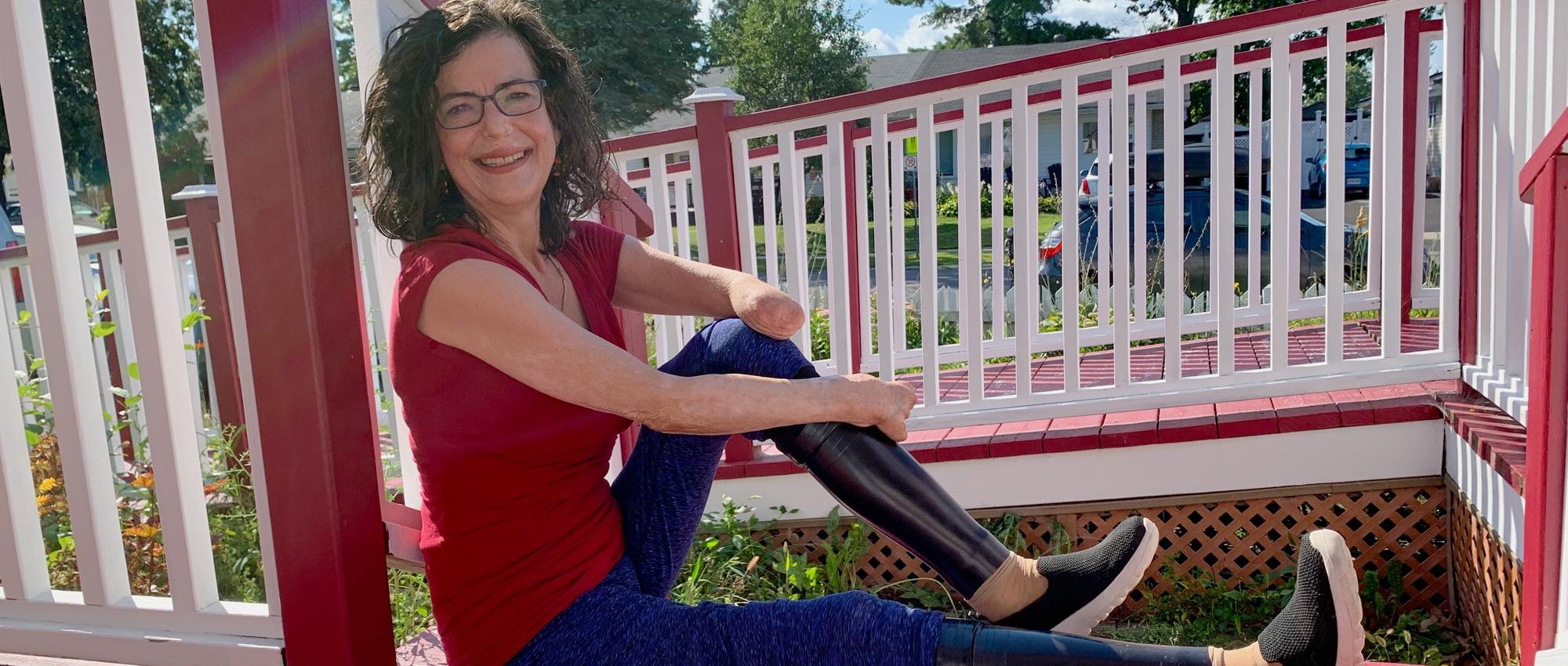 A woman with prosthetic legs sits on her front porch near a wheelchair ramp