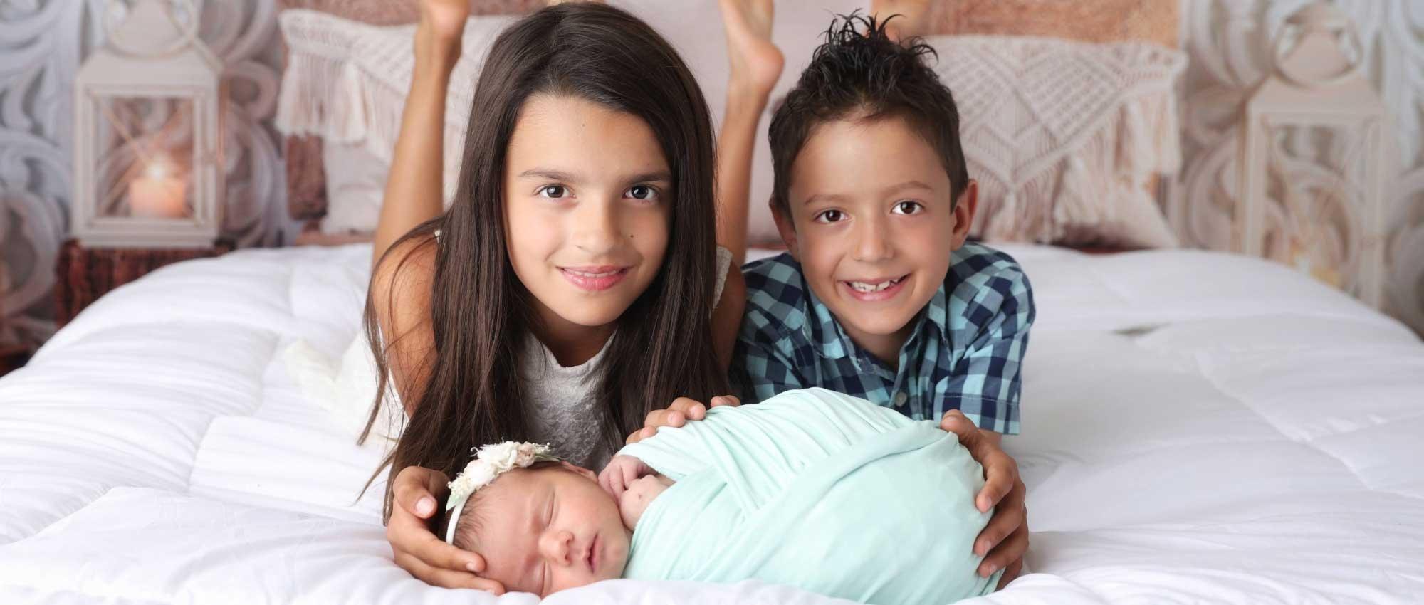 Two children pose with their baby sister
